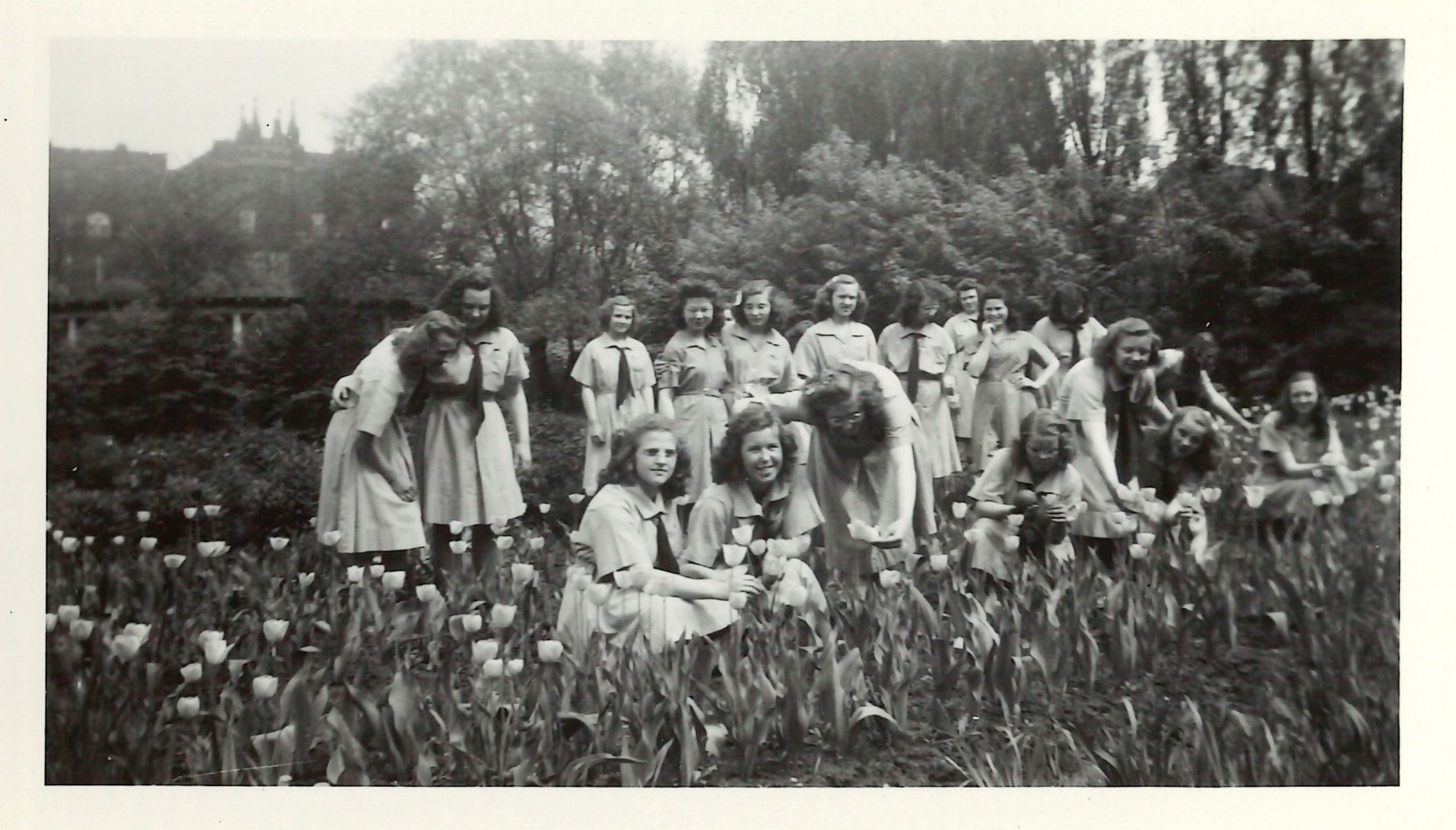 A group of young women in matching dresses in a field of tulips with the back of a tall building behind them.