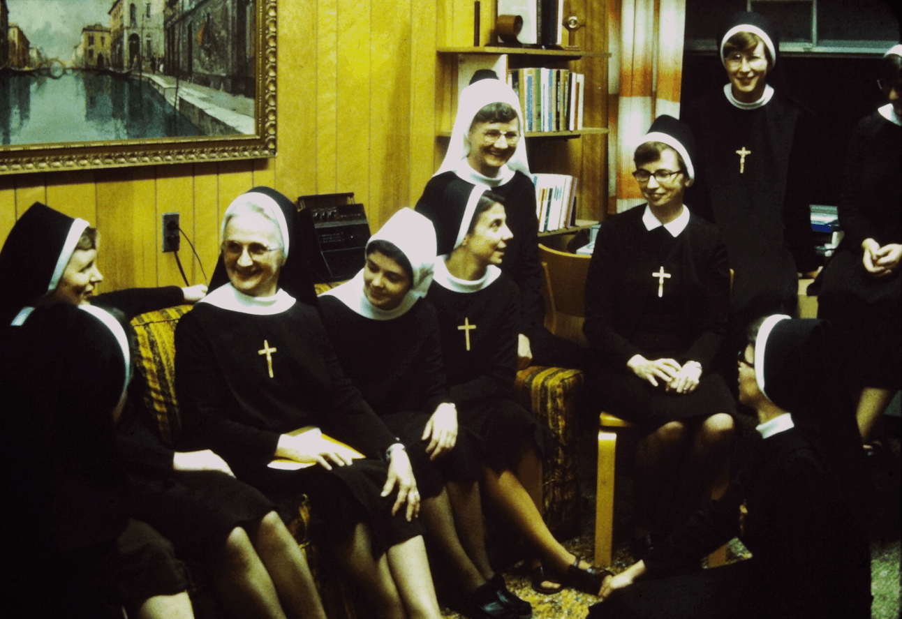 A group of sisters, novices and full fledged sisters, sitting and standing around an office.
