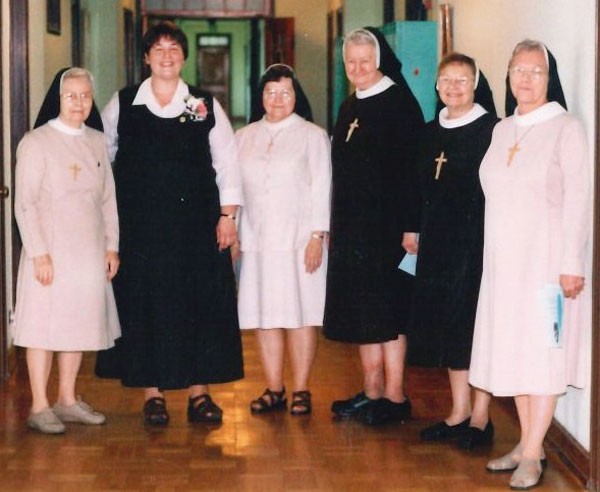 Group of six sisters standing in a hallway. The youngest of them does not wear a veil and has a boutonniere pinned to the front of her dress.